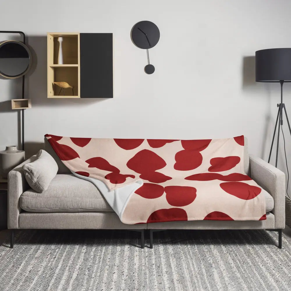 Une couverture rouge et crème en tissu doux avec motifs feuilles rouges abstraites sur un canapé gris