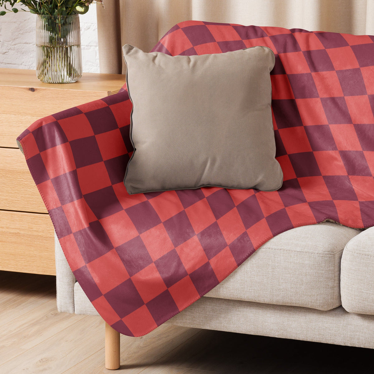 Red checkered blanket in red and maroon plaid draped over a beige sofa for cozy home use
