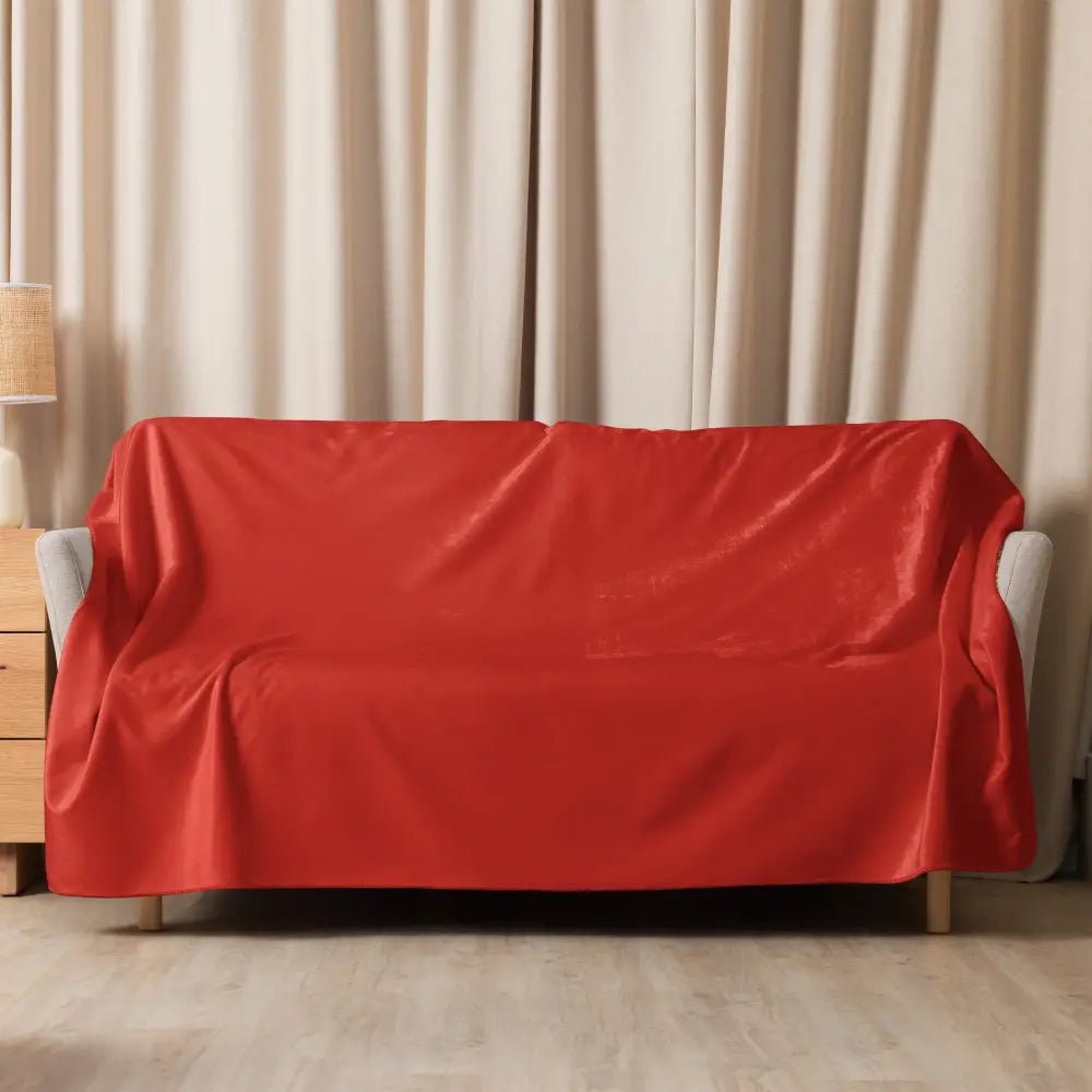 A vibrant red sherpa blanket with plush texture elegantly draped over a modern velvet sofa cover