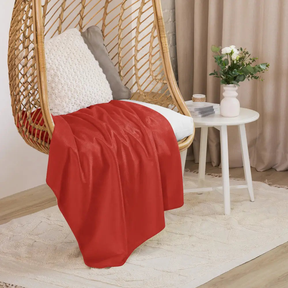 A vibrant red sherpa blanket with smooth texture draped over a wicker hanging chair for cozy comfort
