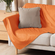 Orange sherpa blanket plush draped over a sofa with a gray pillow for cozy warmth and comfort