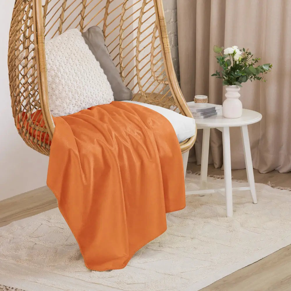 A soft vibrant orange sherpa blanket draped over a wicker hanging chair showcasing its plush texture