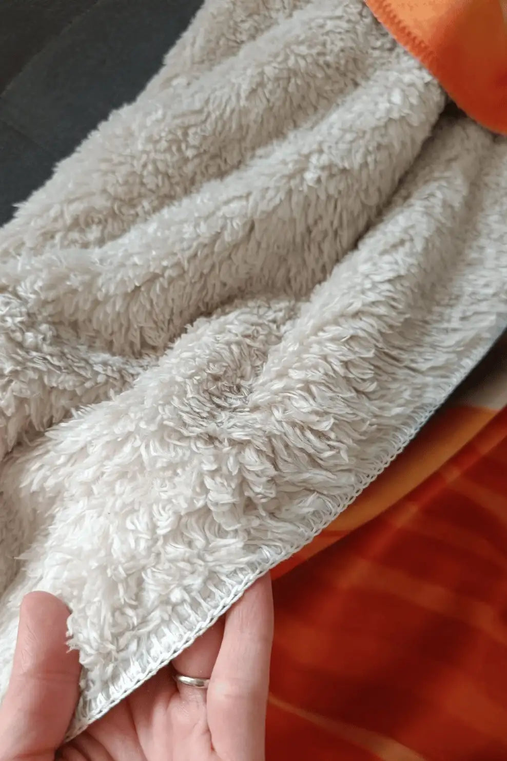 A soft, off-white plush blanket with a textured, curly fleece surface and a neatly finished edge.