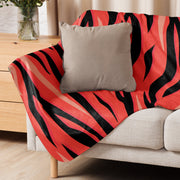 A vibrant red and black tiger stripe throw blanket draped over a beige sofa for cozy home decor