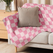 Pink checkered blanket with pink and white pattern draped over a beige sofa showing its front side