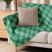 Green checkered blanket in green and dark green draped over a beige sofa made of soft woven fabric