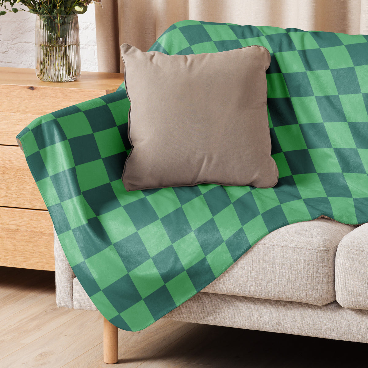 Green checkered blanket in green and dark green draped over a beige sofa made of soft woven fabric