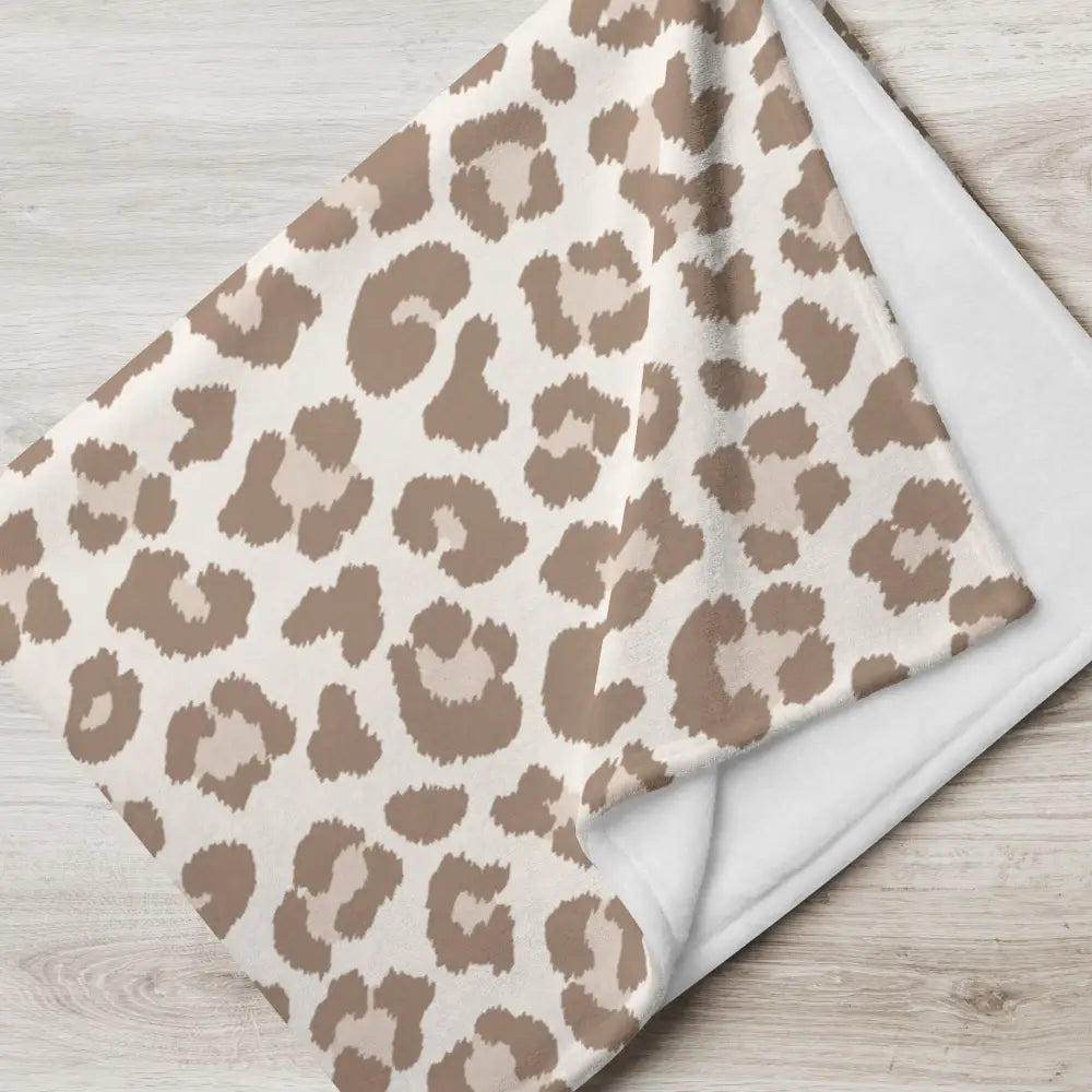 A soft plush tan leopard print blanket with beige and taupe pattern and solid white interior for cozy use