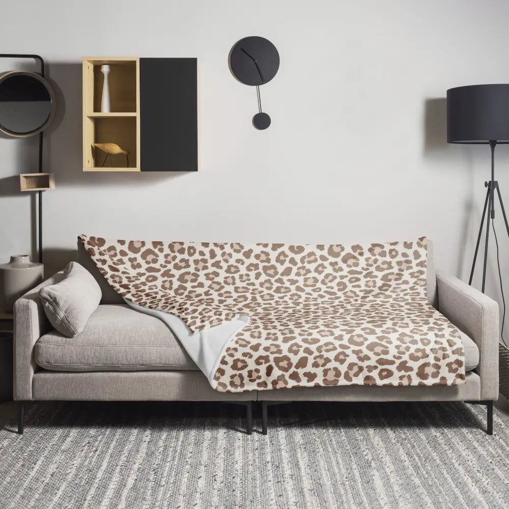 Tan leopard print fleece blanket with soft beige and brown pattern draped over modern gray sofa