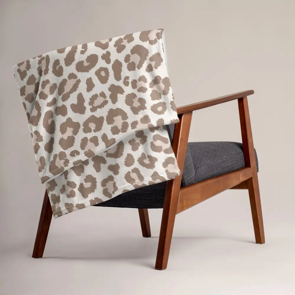 A soft tan leopard print throw blanket in beige and cream draped over a wooden armchair