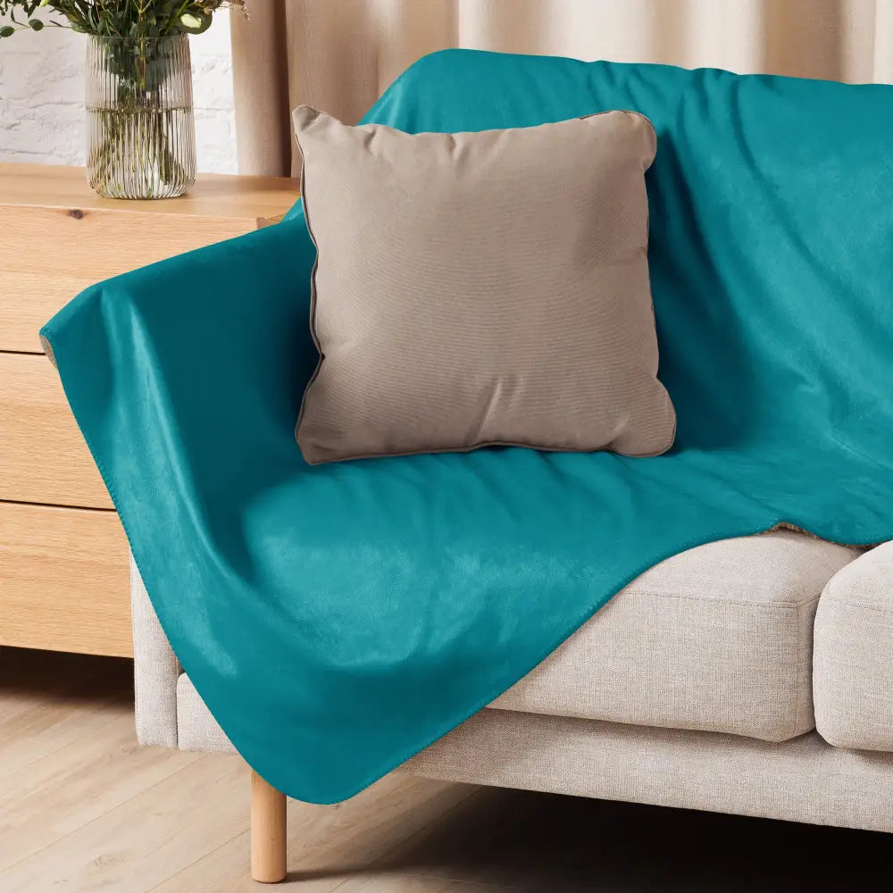 Teal sherpa throw blanket displayed on a teal velvet sofa cover with a beige cushion resting on it