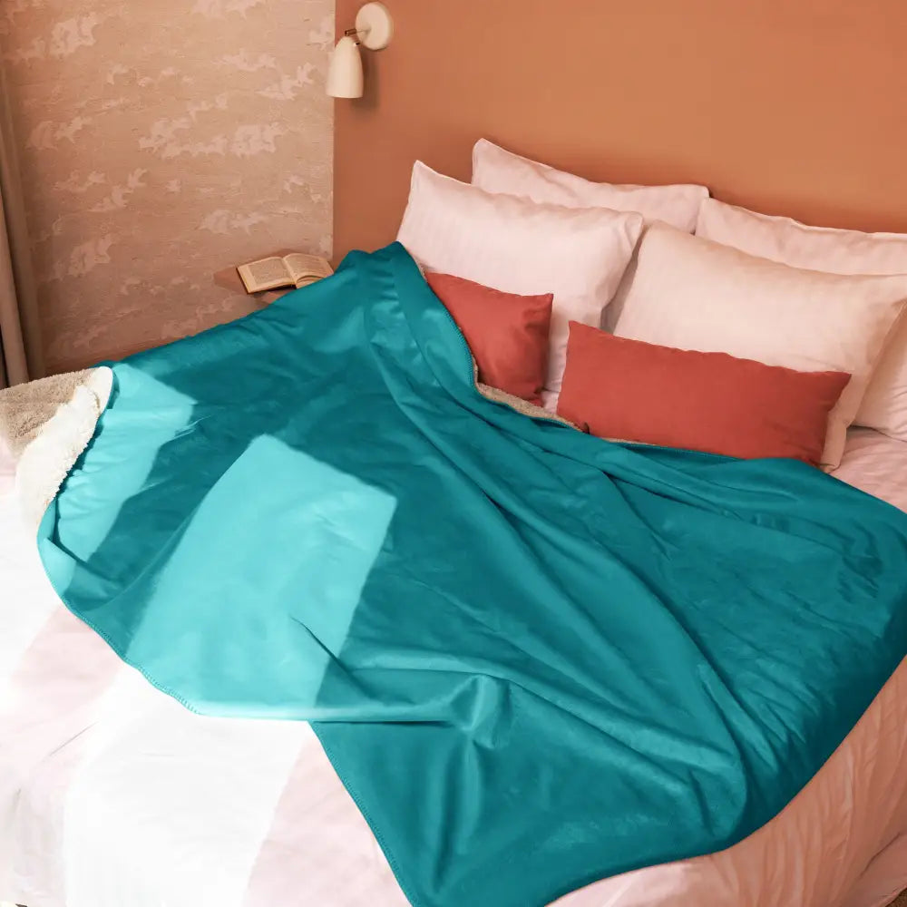 A plush teal sherpa throw blanket with soft slightly shiny fabric draped over a bed for cozy warmth