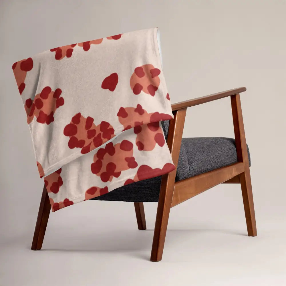 A soft cream-colored throw blanket with red and terracotta abstract flowers draped over a wooden armchair
