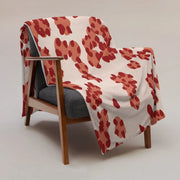A cozy cream-colored throw blanket with bold red and terracotta abstract floral pattern draped over wooden armchair