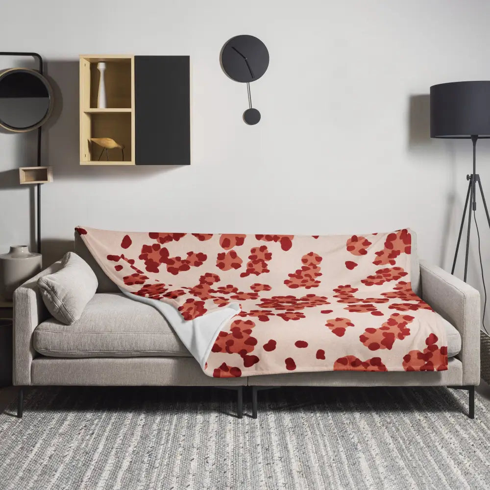 A soft cream-colored throw blanket with vibrant red floral pattern draped over a modern gray sofa