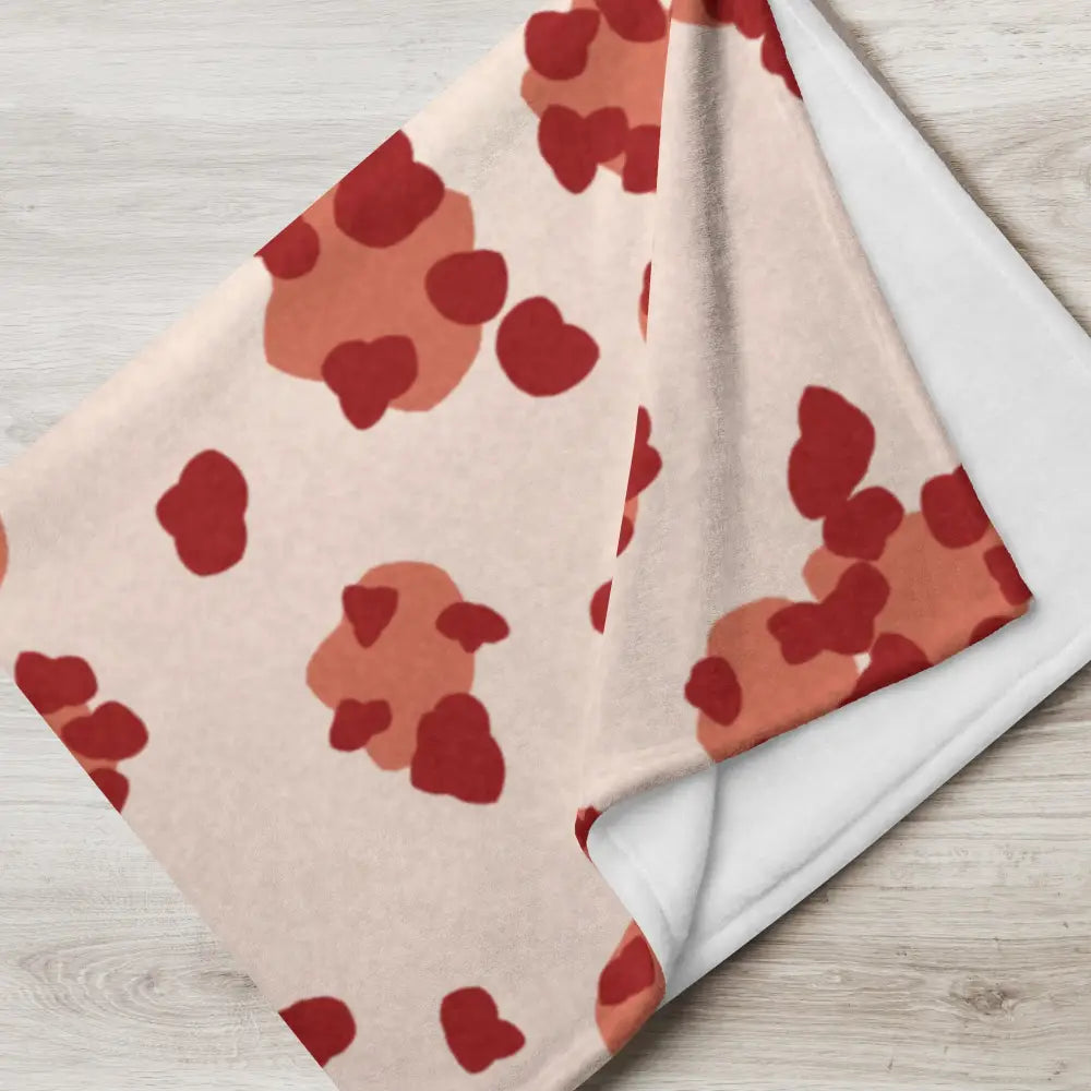 A soft blush-colored throw blanket with red and terracotta heart patterns for cozy home use
