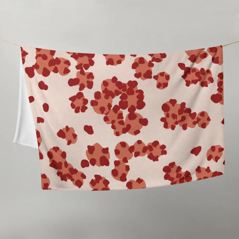 A soft cream-colored throw blanket with a playful pattern of red and terracotta abstract shapes
