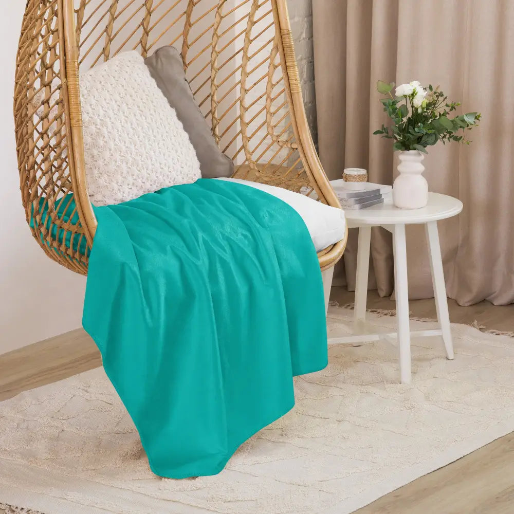 A soft vibrant teal sherpa blanket draped over a wicker hanging chair for cozy indoor use