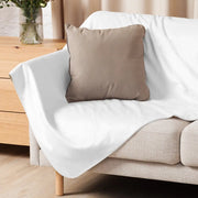 A soft white sherpa fleece blanket draped over a beige sofa with a taupe pillow resting on it