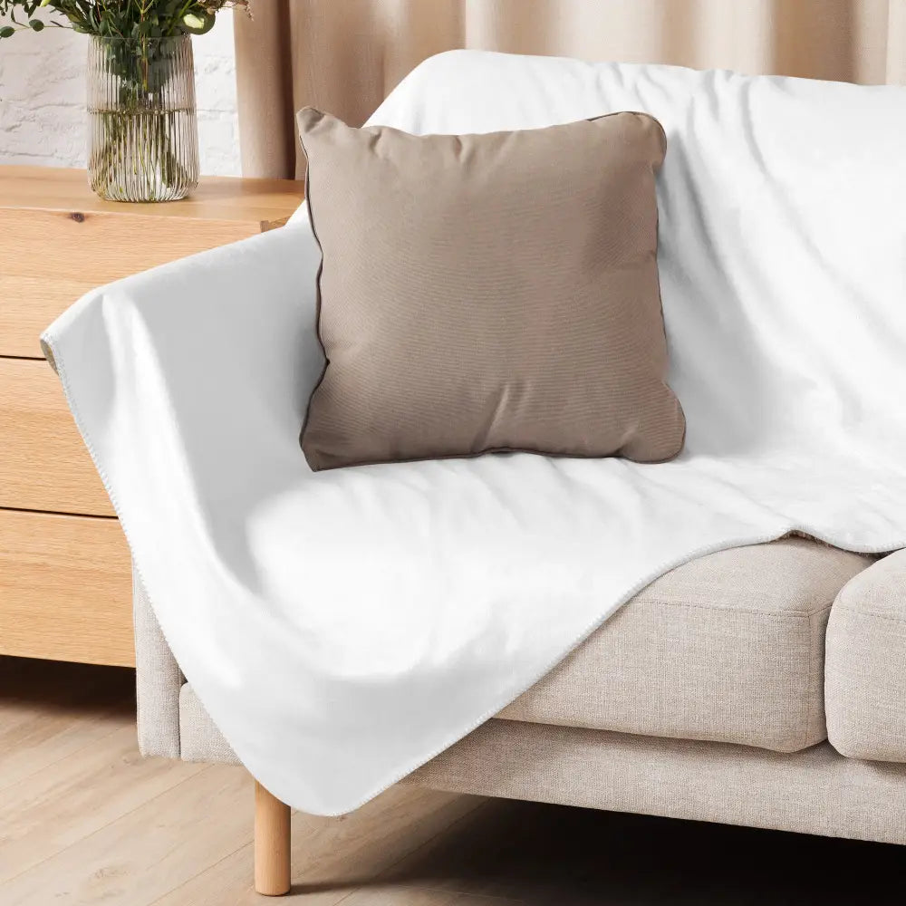 A soft white sherpa fleece blanket draped over a beige sofa with a taupe pillow resting on it