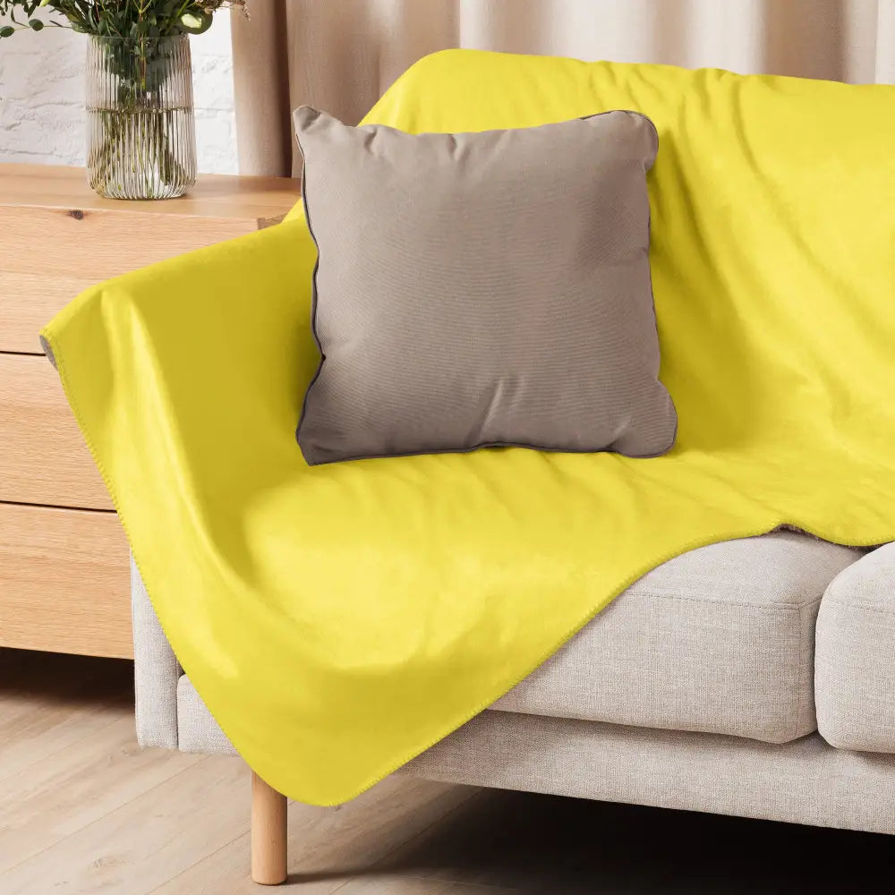 Bright yellow sherpa throw blanket made of fleece draped over a sofa for cozy warmth and comfort